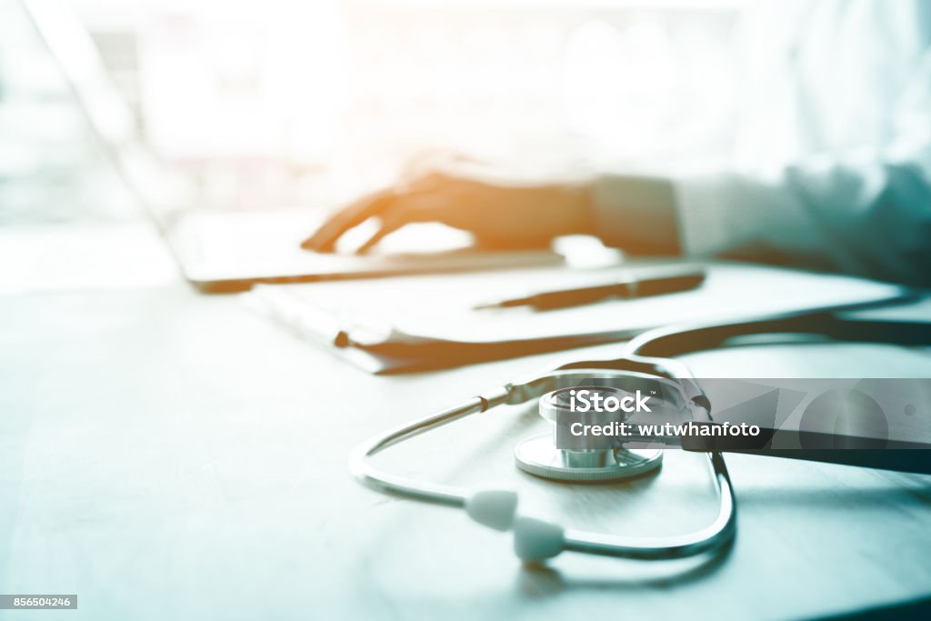 Doctor using laptop at desk in clinic working on computer at room office. Stethoscope Stock Photo