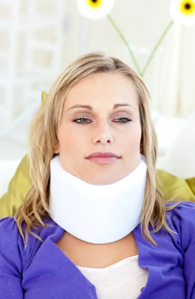 Attractive woman wearing neckbrace lying on a sofa against a white background