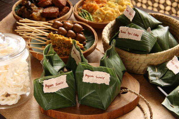 Angkringan Nasi Kucing, a Popular Javanese Street Food of Small Portion of Rice Package with Variety of Toppings and Side Dishes This is the luxury version of Angkringan Nasi Kucing, a popular street food fare of small portion of rice dish in banana leaf package (a portion so small resembling a cat's rice portion, hence the name nasi (rice) kucing (cat)). The rice dish is topped with variety of toppings such as shredded chicken, sautéed tempeh, and sautéed anchovy. Each portion dish is wrapped in banana leaf and grouped together based on the topping. The package is given handwritten label of the topping inside. The rice dish are accompanied with extra side dishes of satays (chicken intestine, quail eggs, cockles), sweet-soy braised food (tofu, tempeh, offal) and fritters (vegetables and tempeh). Some crackers are also provided to complete the meal. The food are arranged on a wooden table lined with recycled papers. central java province photos stock pictures, royalty-free photos & images