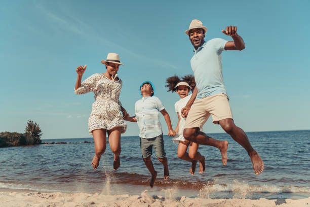 family on beach happy african american family holding hands and jumping on beach 2012 stock pictures, royalty-free photos & images