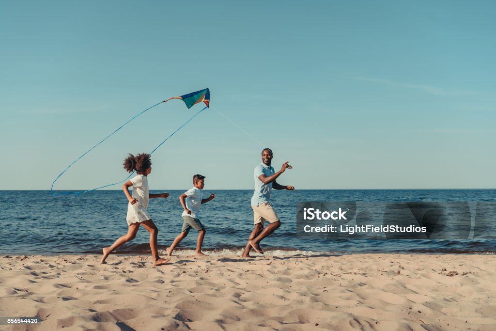 father and kids playing with kite on beach happy african american father and kids playing with kite on beach Beach Stock Photo