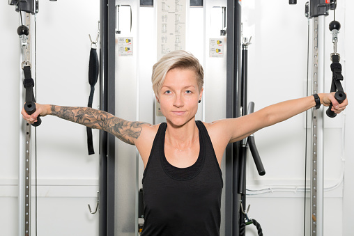 Tattooed young lady in a black tank top using a cable weight machine