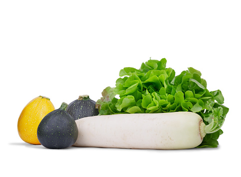 A close-up of bright zucchinis next to green salad leaves and white turnip isolated on a white background. Organic autumn vegetables full of vitamins. Natural ingredients for salads.