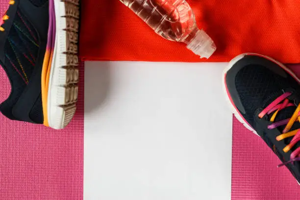 Sports accessories on a pink background. Sneakers, water bottle, t-shirt. A clean sheet for notes