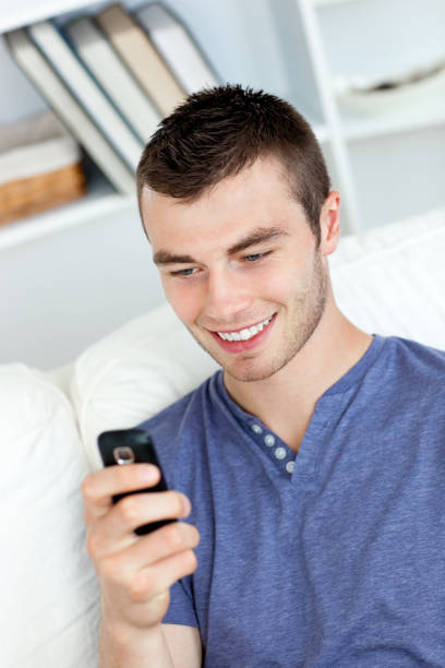istock Charming young man sending a text and smiling in the livingroom 856586010