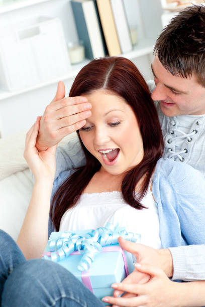 istock Handsome boyfriend giving a present to his surprised girlfriend on a sofa 856615052