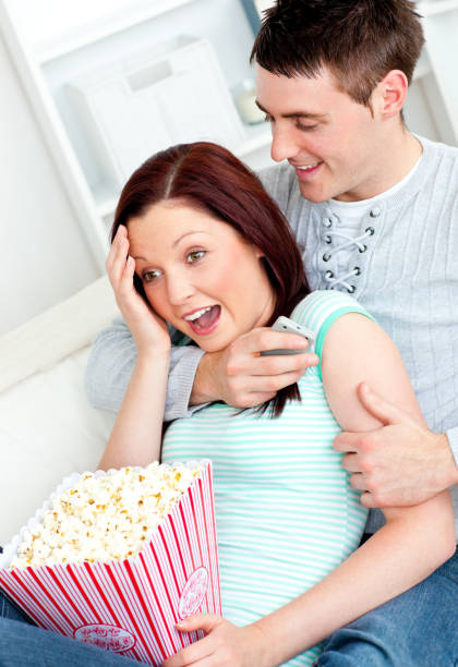 Young couple lying on the sofa with popcorn and remote Young couple lying on the sofa with popcorn and remote at home woman strangles man stock pictures, royalty-free photos & images