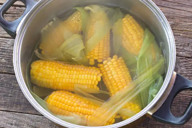 Cooked corn cobs in pot on wooden table