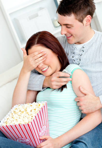 Charming couple lying on the sofa with popcorn and remote Charming couple lying on the sofa with popcorn and remote at home woman strangles man stock pictures, royalty-free photos & images