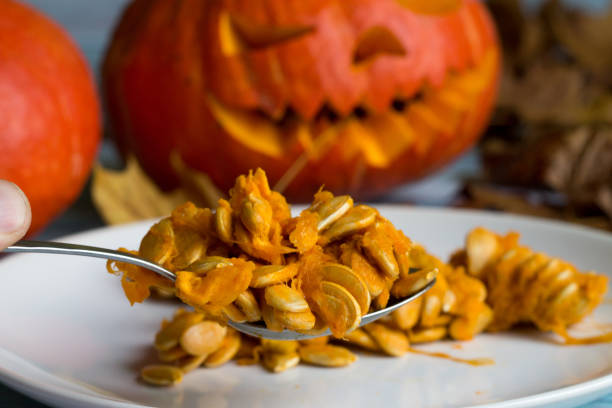 Halloween. All Saints' Day. pumpkin seeds on the white plate on the background of Jack O 'Lanterns. Halloween. All Saints' Day. pumpkin seeds on the white plate on the background of Jack O 'Lanterns. throwing up pumpkin stock pictures, royalty-free photos & images