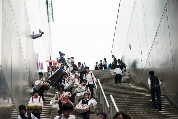 Commuters, large group of people,  go down the stairs at the Kyoto Station, security camera on the wall. Japan