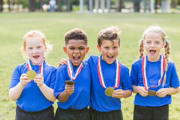 Multi-ethnic children on winning team, with medals A group of four multi-ethnic children, 6 and 7 years old, on the winning team. They are smiling at the camera, holding up the medals that are on ribbons around their necks. multi medal stock pictures, royalty-free photos & images