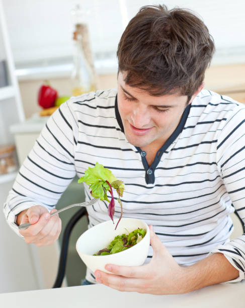 istock Delighted young man eating a healthy salad in the kitchen 856718036