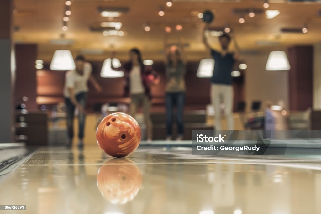 Friends playing bowling Happy young friends are having fun while playing bowling together, ball in focus Activity Stock Photo