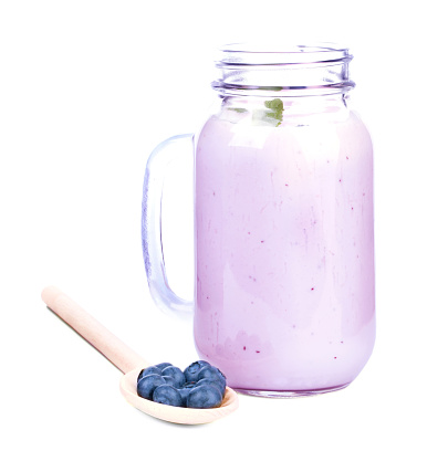 A big mason jar full of healthful pink smoothie from berries, isolated on a white background. A little light brown wooden spoon with some sweet and organic blueberries. Copy space.