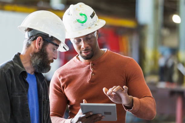 zwei arbeiter tragen schutzhelme mit digital-tablette - manual worker portrait helmet technology stock-fotos und bilder