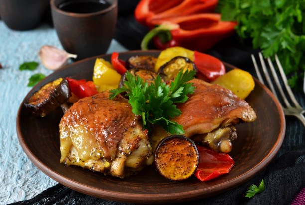 A hearty meal. Chicken thighs baked with potatoes, peppers and aubergines on a blue concrete background stock photo
