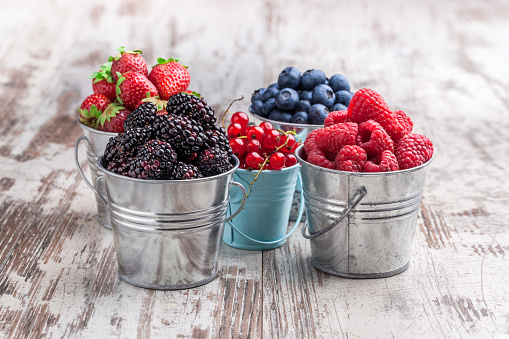 Colorful berries assortment in five tin cans on rustic wooden table blueberry, raspberry, red currant, strawberry, in five old tin cans on rustic wooden table in studio