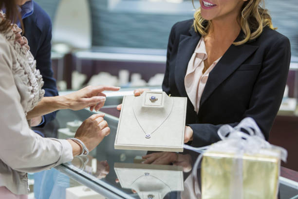 Saleswoman helping couple in jewelry store Cropped view of a saleswoman in a jewelry store helping a mature couple, showing the female customer a ring and necklace from the display case. display cabinet photos stock pictures, royalty-free photos & images