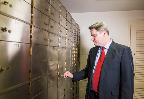 Mature man wearing a business suit locking or unlocking a safety deposit box.