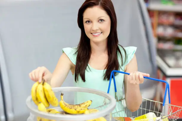 Healthy woman with shoppingbasket buying bananas in a grocery store smiling to the camera