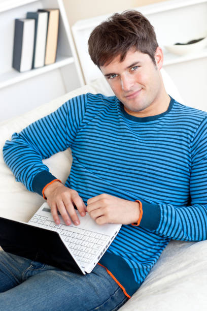 istock Cheerful young man working on his laptop lying on the couch 856780128