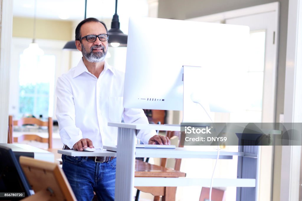 ラテン系アメリカ人ビジネスマンが自宅のコンピューターのデスクを立ってを勤務します。 - スタンディングデスクのロイヤリティフリーストックフォト