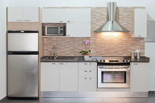 Small or compact modern kitchen with appliances. Contemporary style. Sparse design. White cabinets. Example of design for small architectural spaces. Front view, horizontal composition. Kitchen background.