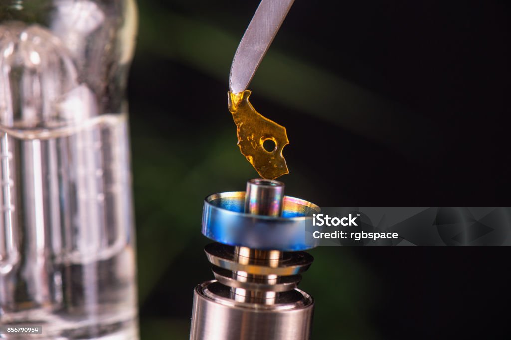 Dabbing tool with small piece of cannabis oil aka shatter - medical marijuana concentrates concept Macro detail of dabbing tool with small piece of cannabis oil aka shatter suspended over a metal rig - medical marijuana concentrates concept Dab - Dance Stock Photo
