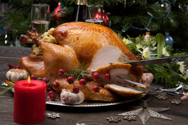 Carving Rustic Style Christmas Turkey Carving rustic style roasted Christmas turkey garnished with roasted garlic, lemon, and rosehips. Surrounded with rustic Christmas ornaments, candles, wine, flowers, and Christmas tree in the background."n carving food photos stock pictures, royalty-free photos & images