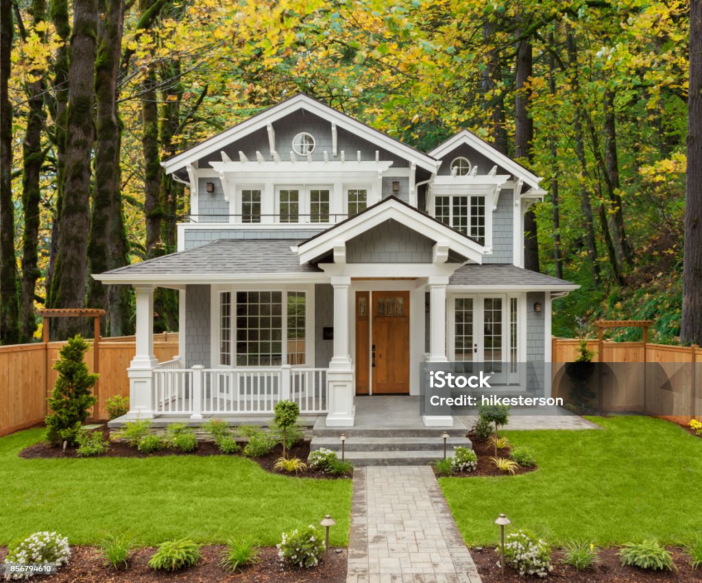 Beautiful Luxury Home Exterior with Green Grass and Landscaped yard. Colorful Forest forms Backdrop of Home. new luxury home with elegant touches including covered entrance, and columns House Stock Photo