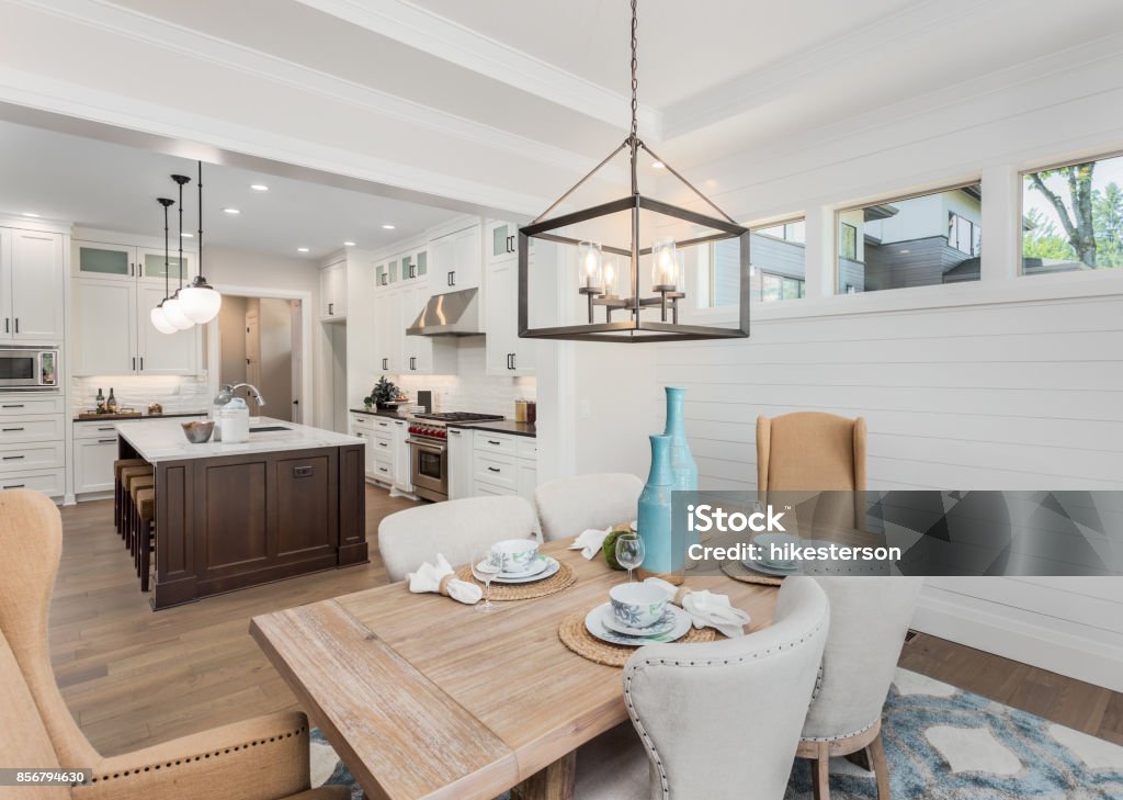 Beautiful Dining Room and Kitchen in Luxury Home Dining Room and Kitchen Interior in New Luxury Home: Kitchen has Island, Sink, Cabinets, and Hardwood Floors. Dining Room has table with place settings. Pendant Lights accent Both Rooms Dining Room Stock Photo