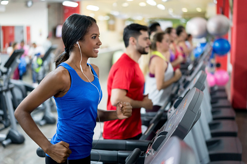 Athletic woman at the gym running on the treadmill and listening to music with headphones - fitness concepts