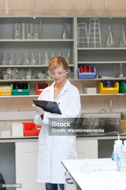 Concentrated Female Scientist Writing On Her Clipboard Stock Photo - Download Image Now