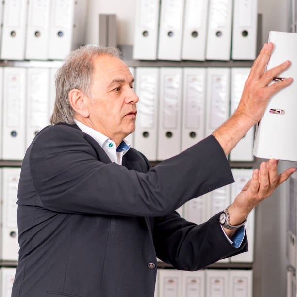 Older man with white shirt puts a documents folder on a shelf Elderly man with a white shirt puts a document folder on a shelf fähigkeit stock pictures, royalty-free photos & images