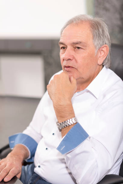 Smiling older man with white shirt Smiling older man with a white shirt sits at a desk fähigkeit stock pictures, royalty-free photos & images