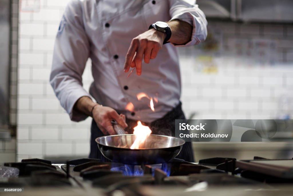 A man cooks cooking deep fryers in a kitchen fire. A man cooks cooking deep fryers in a kitchen fire. He gently fry the vegetables while cooking the dish. Chef Stock Photo