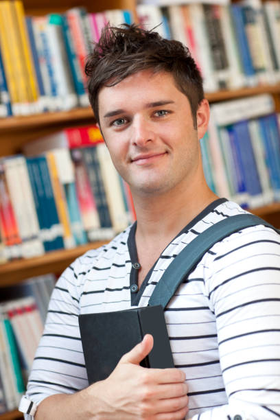 istock Portrait of a smart student holding a book standing in the library 856873368