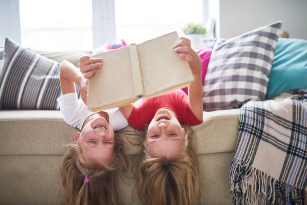 sorelle che leggono libro a testa in giù - famiglia con due figli foto e immagini stock