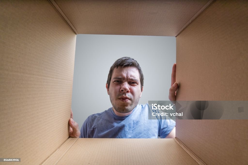 Young disappointed man is looking on gift inside cardboard box. Gift Stock Photo