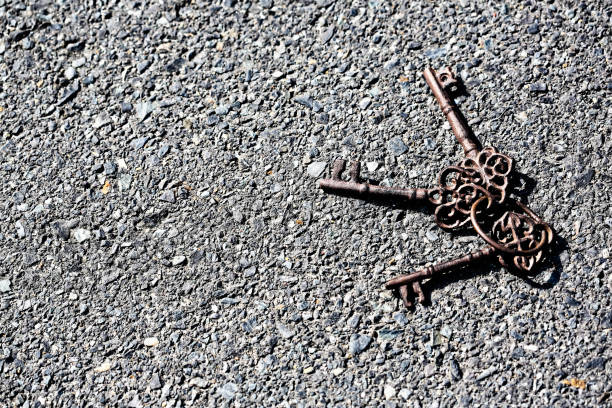 Three old, rusted keys on a keyring lie outdoors on the asphalt road surface.
