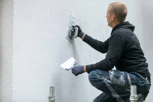 Photo of construction worker putting decorative plaster on house exterior