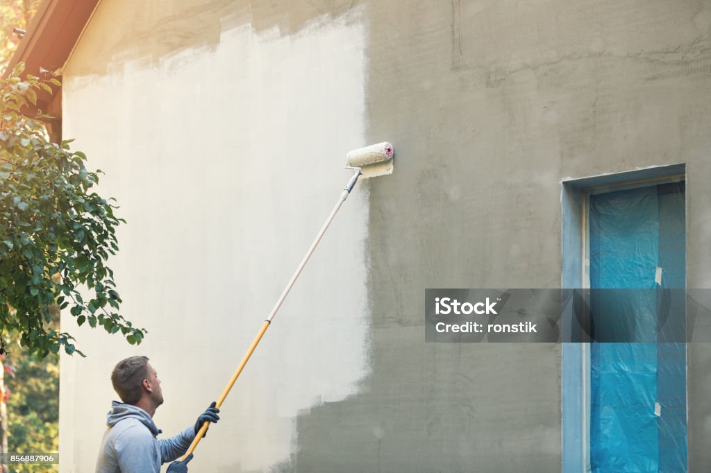 house painter painting building exterior with roller Painting - Activity Stock Photo