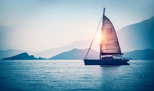 Sailboat in the sea in the evening sunlight over beautiful big mountains background, luxury summer adventure, active vacation in Mediterranean sea, Turkey