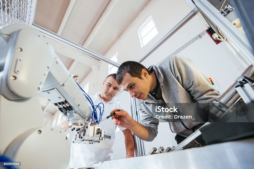 Precise mechanics on robotic arm in industry Engineers working on development of automated production line with robotic parts and applied software in order to increase productivity. Precise engineering on electric parts of automated production line. Engineer Stock Photo