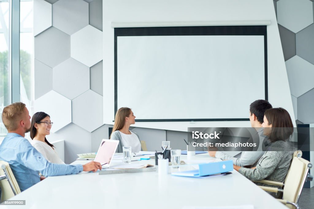 Web conferencing with business partner Group of smiling business colleagues watching video presentation on projection screen while they thinking of project at conference Projection Screen Stock Photo