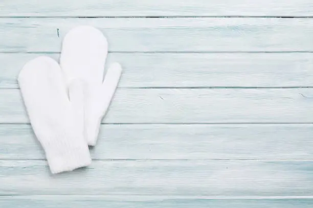 White mittens on wooden table. Christmas background. Top view with copy space