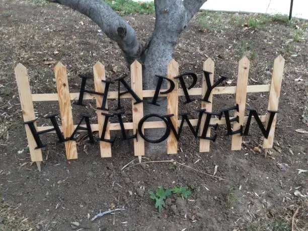 A large garden/yard sign saying "Happy Halloween". Resting on a tree.