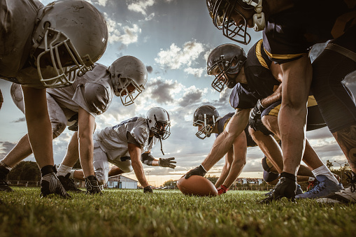 American football on field in stadium with dramatic spot lighting and copy space. Focus on foreground ball with shallow depth of field on background.