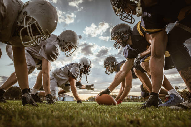Below view of American football players on a beginning of the match. Low angle view of American football players confronting before the beginning of a match. american football sport stock pictures, royalty-free photos & images